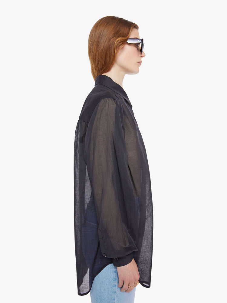 Side view of woman in a sheer black  collared button-up blouse with long balloon sleeves, a curved hem and an oversized fit. 