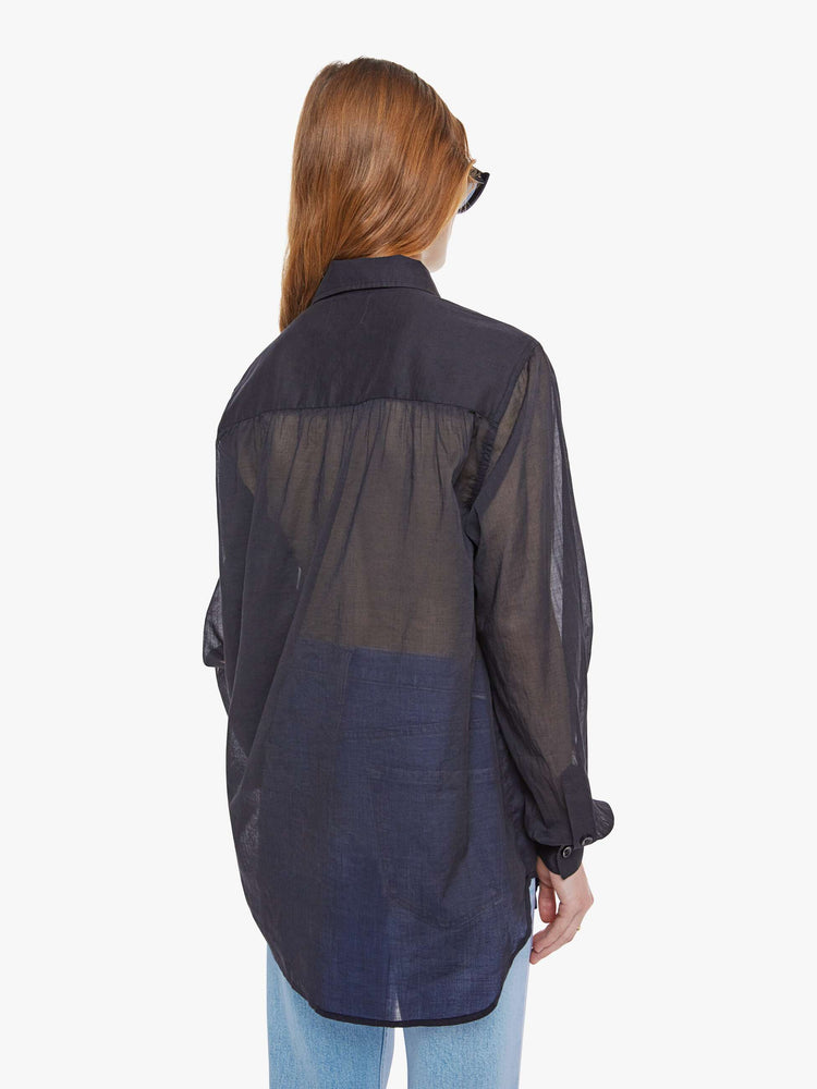Back view of woman in a sheer black  collared button-up blouse with long balloon sleeves, a curved hem and an oversized fit. 