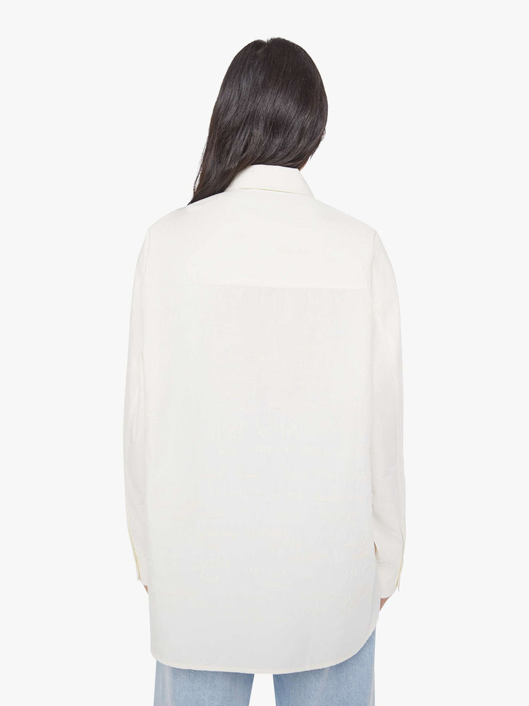 Back view of a woman in an antique white with a chain stitched MOTHER on front and back oversized button-up blouse with drop shoulders and a curved hem.