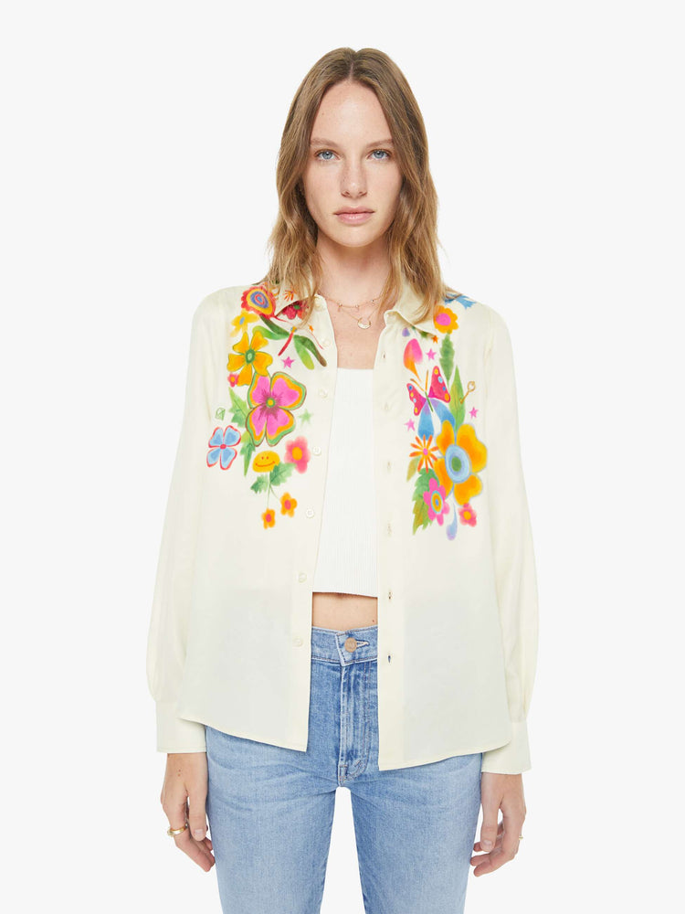 Front view of a woman in an off white with colored flowers collared button-up with long gathered sleeves and a cropped, curved hem.