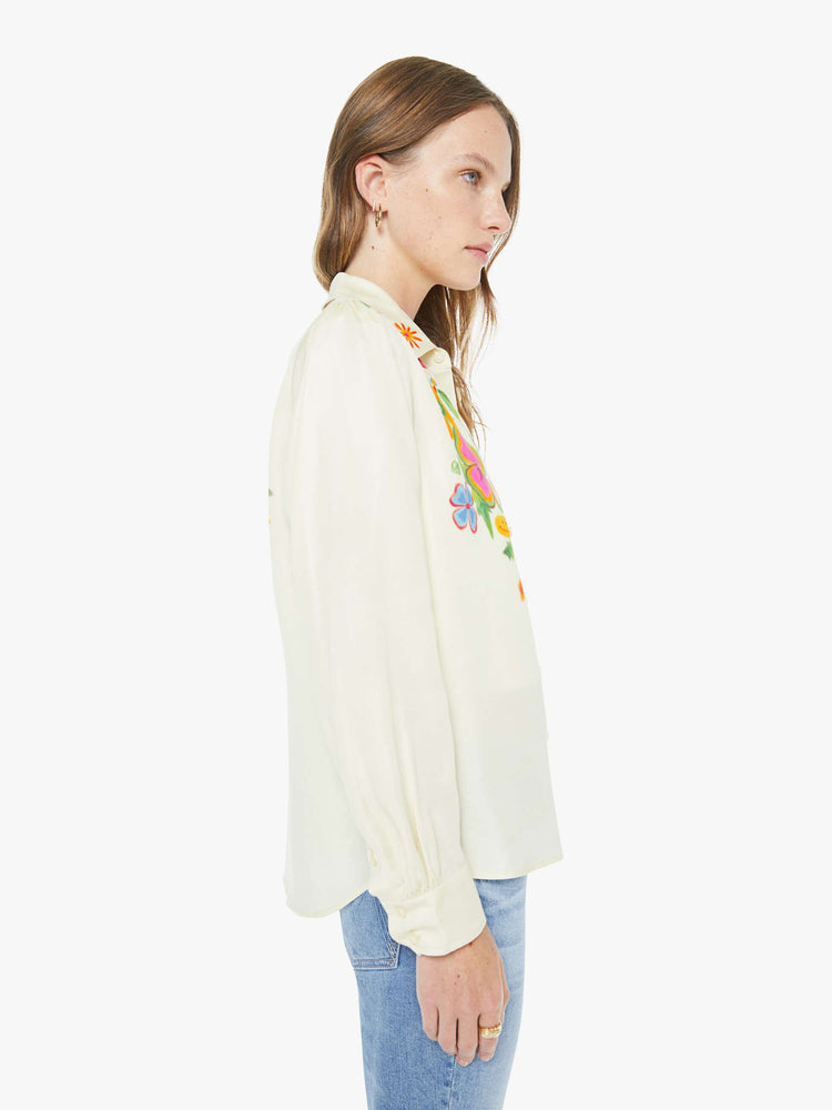 Side  view of a woman in an off white with colored flowers collared button-up with long gathered sleeves and a cropped, curved hem.