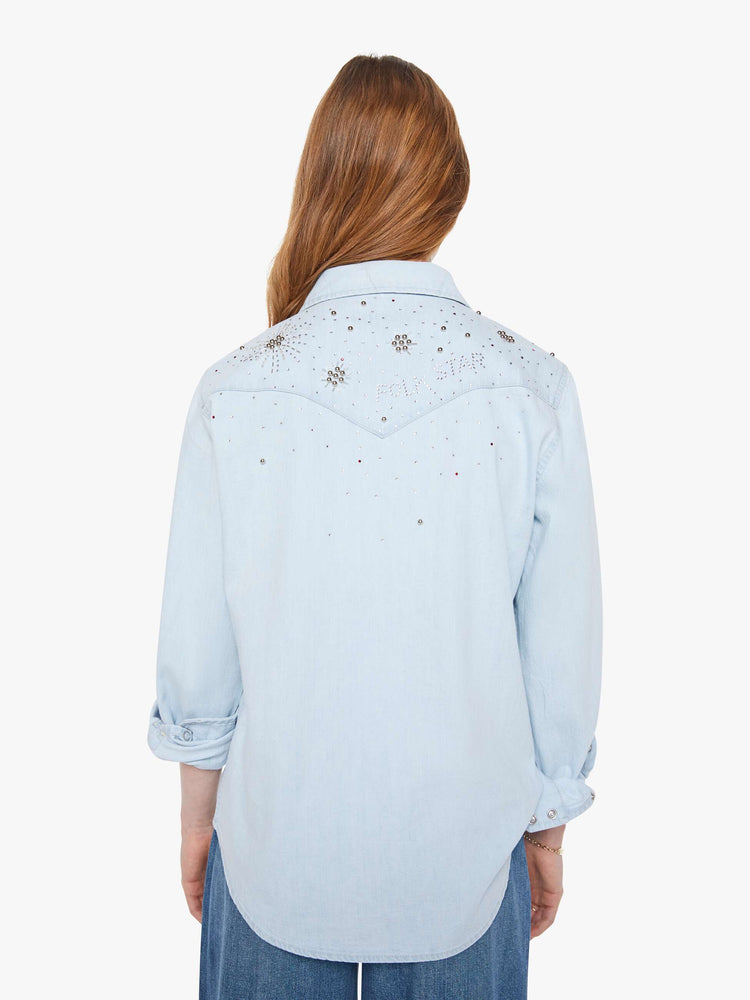 Back view of a woman in a faded light blue with faux pearl snaps down the front and beaded details with rhinestones across the shoulders and chest denim button-up with front patch pockets and a curved hem.