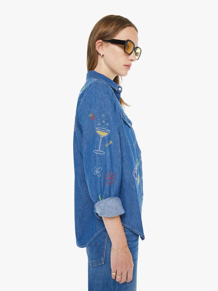 Left side view of a woman in a classic blue denim button-up with front patch pockets and a curved hem.