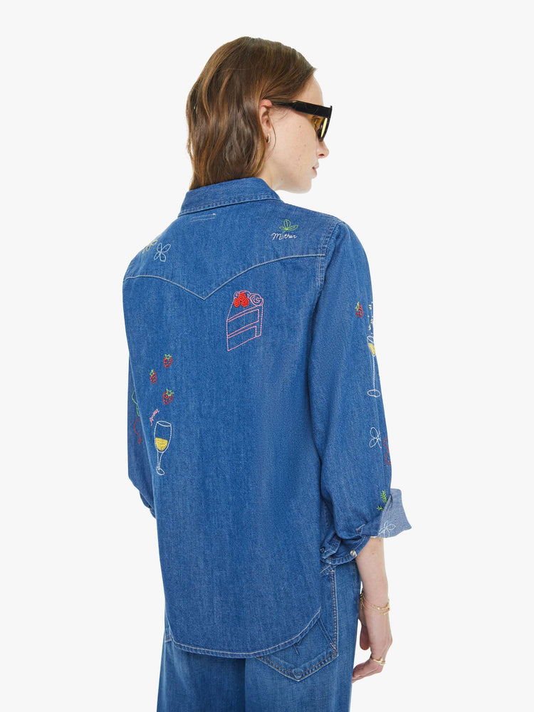 Back view of a woman in a classic blue denim button-up with front patch pockets and a curved hem.