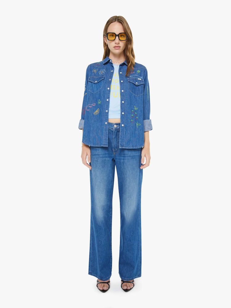 Full body view of a woman in a classic blue denim button-up with front patch pockets and a curved hem.