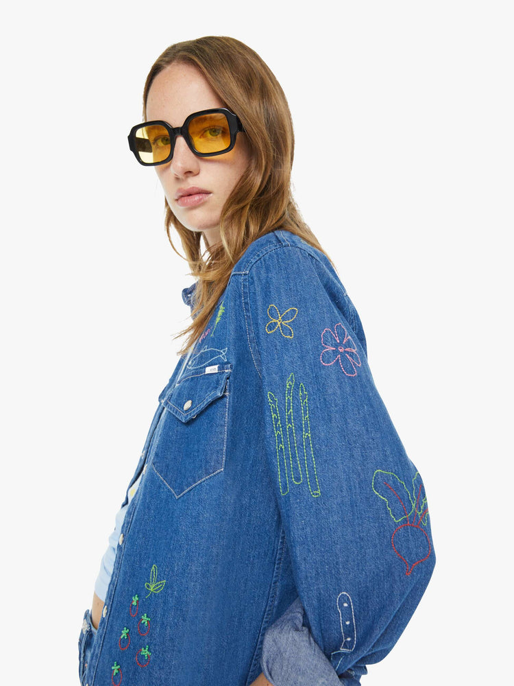 Close up view of a woman in a classic blue denim button-up with front patch pockets and a curved hem.