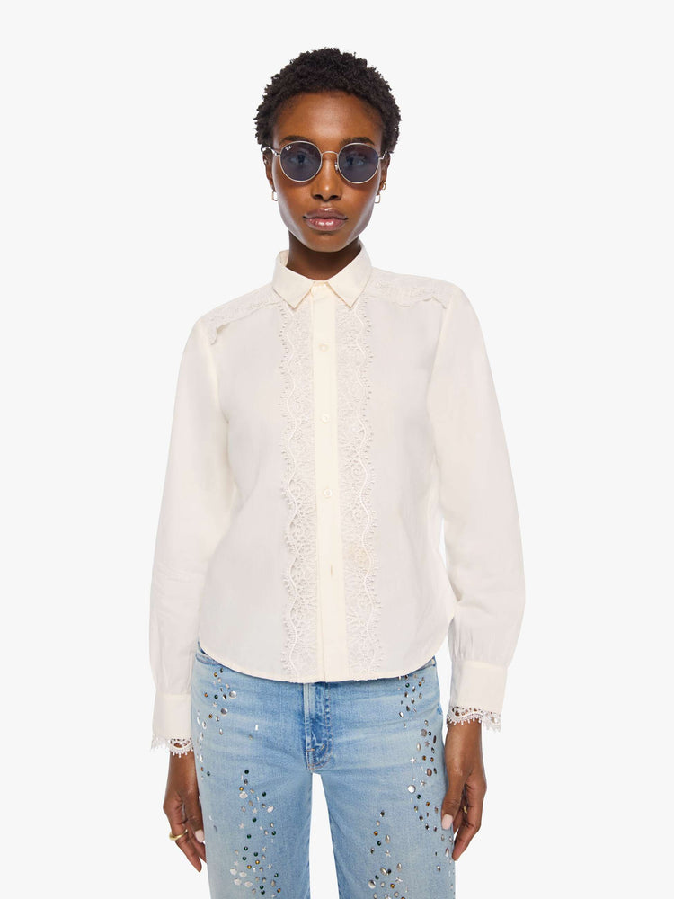 Front view of a woman in top is designed in off-white button-up with a pointed collar, long balloon sleeves and a curved, cropped hem with eyelet-embroidered ruffles down the front, across the shoulders and at the wrists.