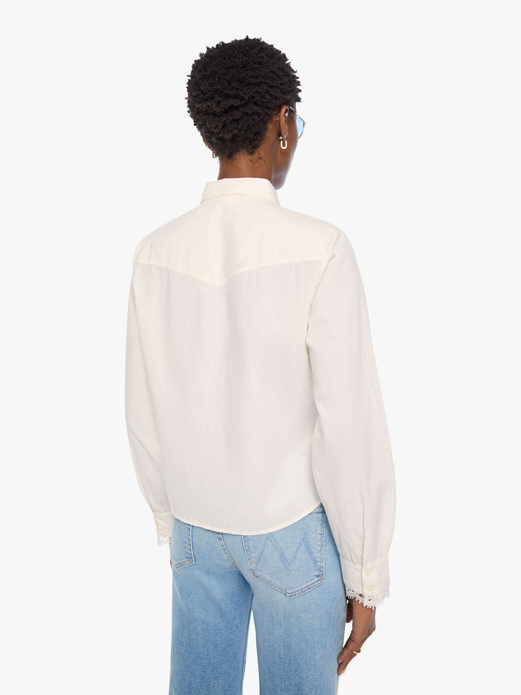 Back view of a woman in top is designed in off-white button-up with a pointed collar, long balloon sleeves and a curved, cropped hem with eyelet-embroidered ruffles down the front, across the shoulders and at the wrists.
