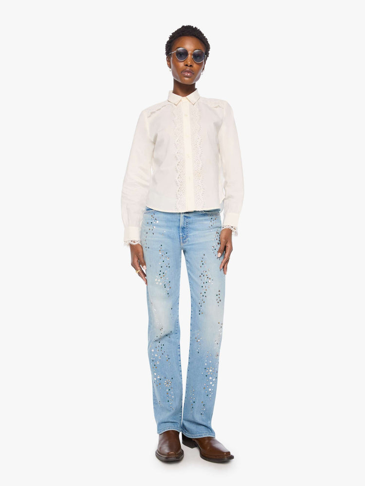 Full body view of a woman in top is designed in off-white button-up with a pointed collar, long balloon sleeves and a curved, cropped hem with eyelet-embroidered ruffles down the front, across the shoulders and at the wrists.