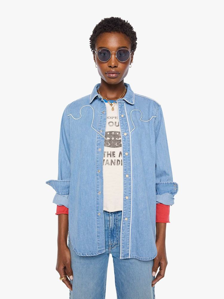 Front view of a woman in light blue oversized denim button-up with drop shoulders, front patch pockets, a Western-inspired yoke and a curved hem.