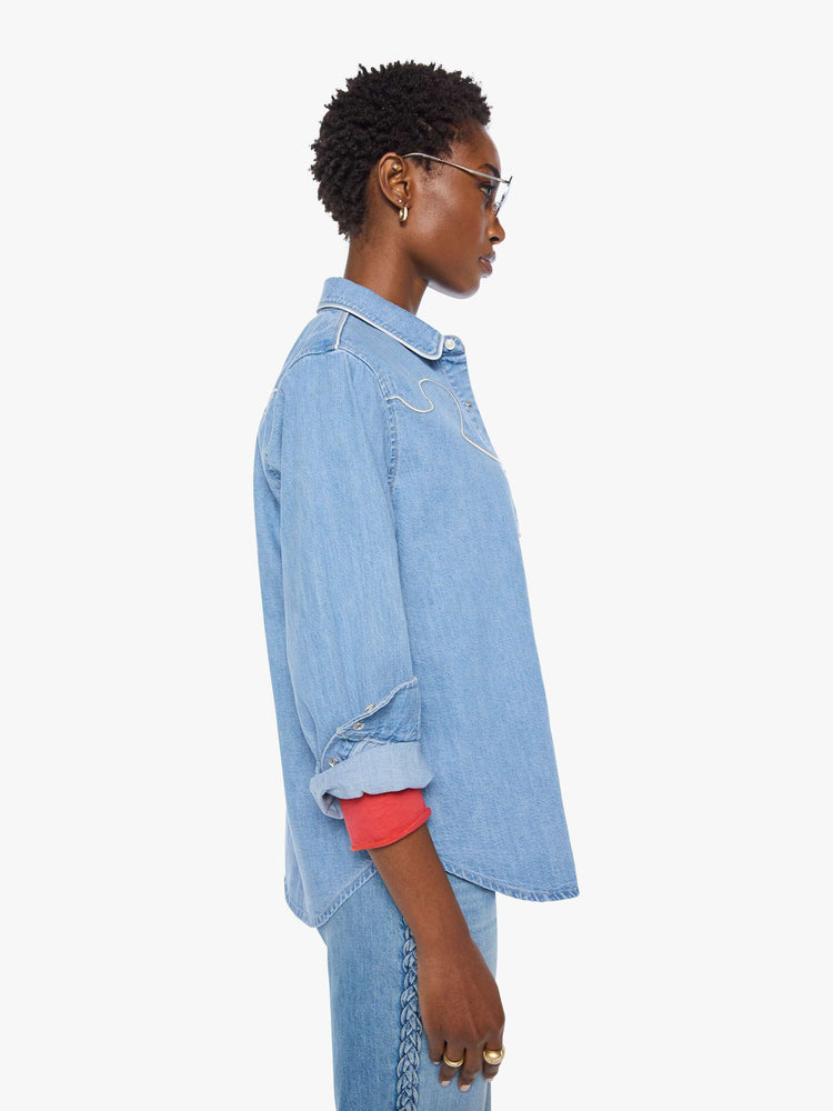 Side view of a woman in light blue oversized denim button-up with drop shoulders, front patch pockets, a Western-inspired yoke and a curved hem.