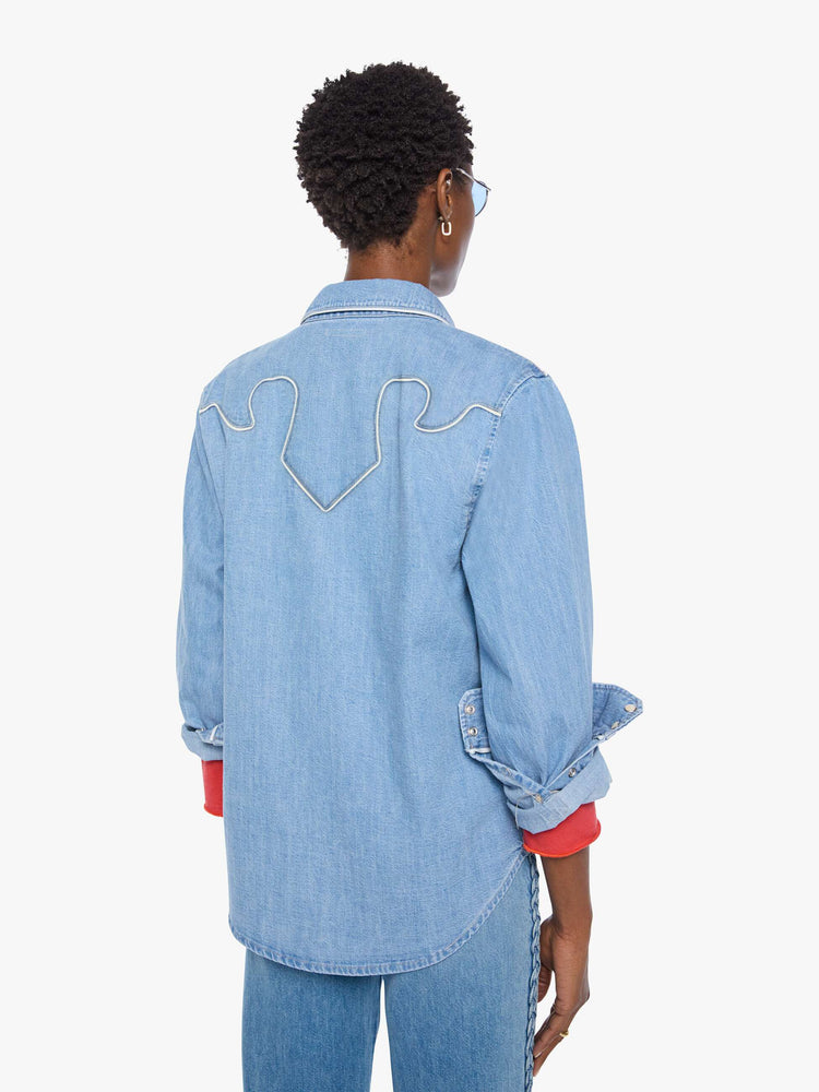 Back view of a woman in light blue oversized denim button-up with drop shoulders, front patch pockets, a Western-inspired yoke and a curved hem.