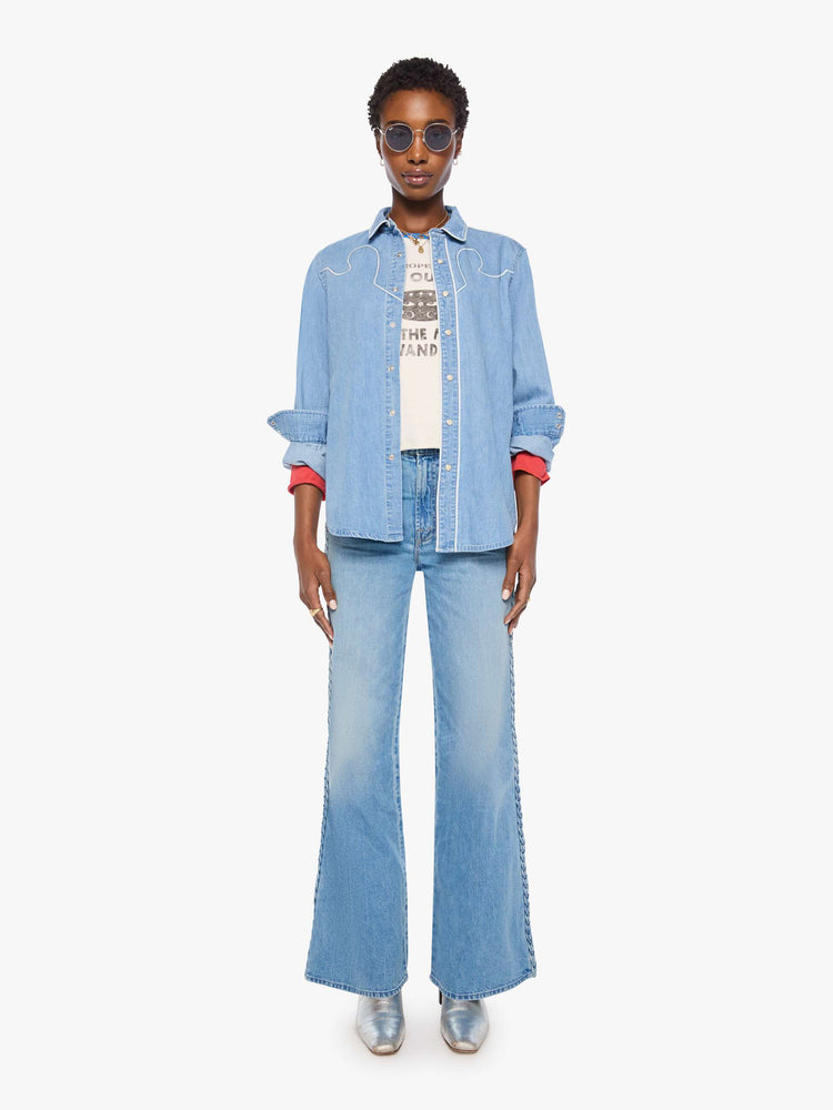 Full body view of a woman in light blue oversized denim button-up with drop shoulders, front patch pockets, a Western-inspired yoke and a curved hem.