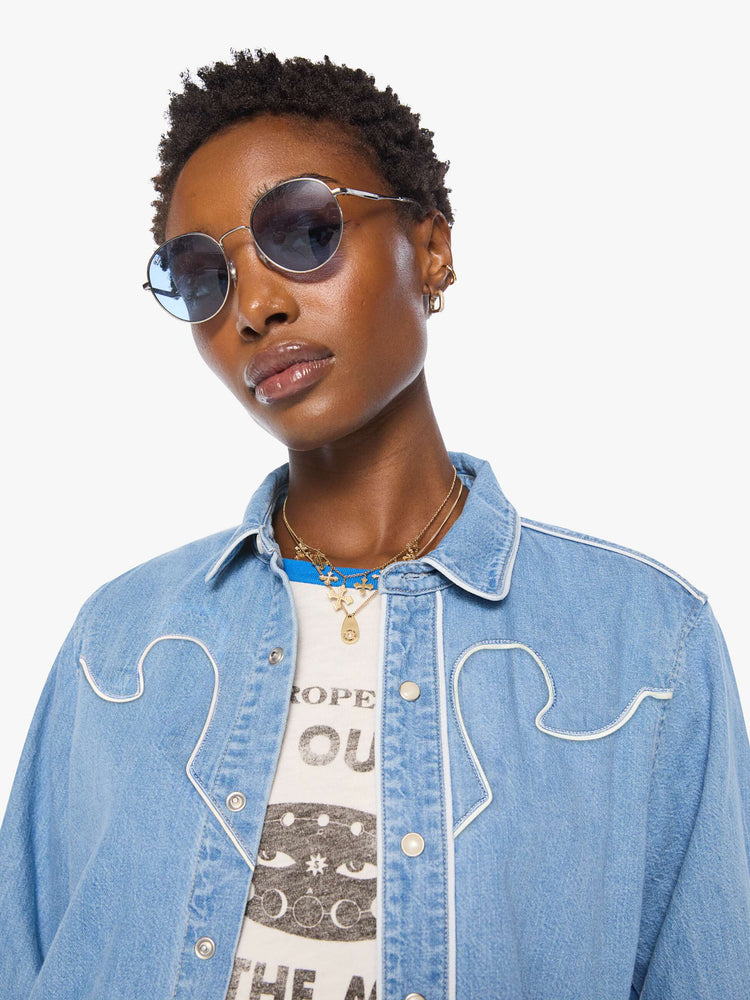 Close up view of a woman in light blue oversized denim button-up with drop shoulders, front patch pockets, a Western-inspired yoke and a curved hem.