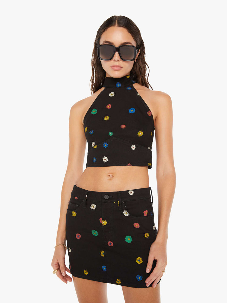 Front view of a woman denim halter top with a mock neck, back-zip closure, darts and angled seams at the chest in black with colorful flowers printed throughout.