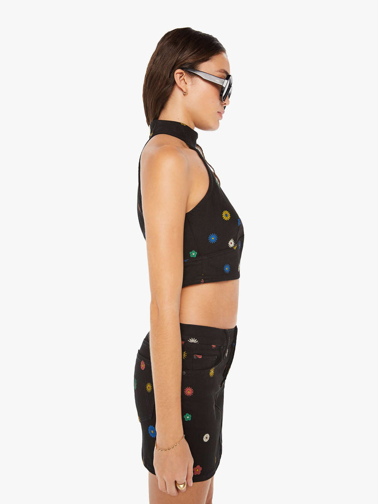Side view of a woman denim halter top with a mock neck, back-zip closure, darts and angled seams at the chest in black with colorful flowers printed throughout.