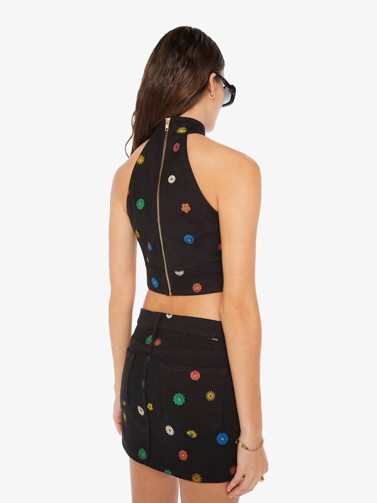 Back view of a woman denim halter top with a mock neck, back-zip closure, darts and angled seams at the chest in black with colorful flowers printed throughout.