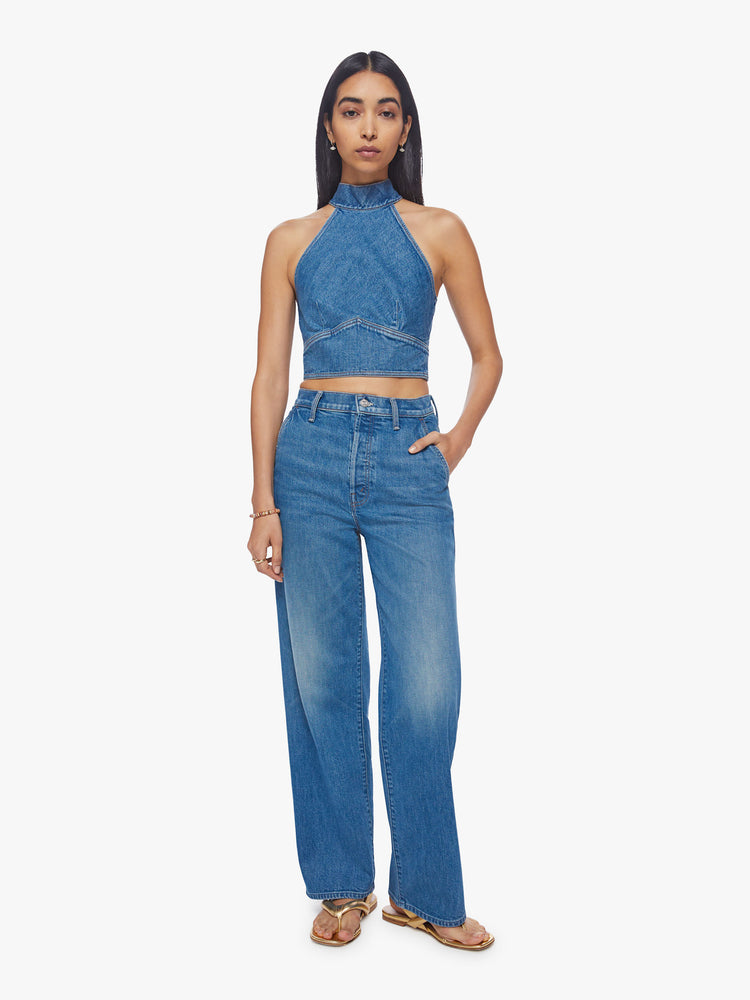 Full body view of a woman denim halter top with a mock neck, back-zip closure, darts and angled seams at the chest in a mid-blue wash.