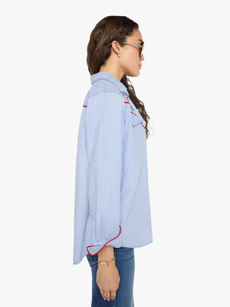 Side view of a woman in a light blue classic button-up shirt with a curved hem and a loose fit.