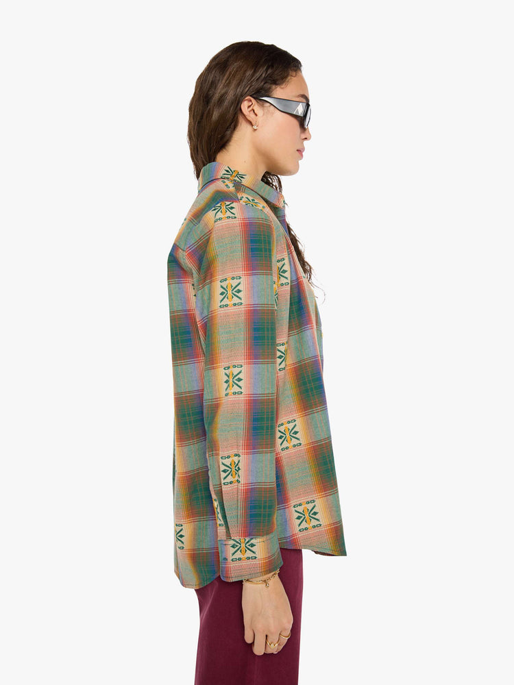 Side view of a woman in  plaid with embroidered details throughout button up.