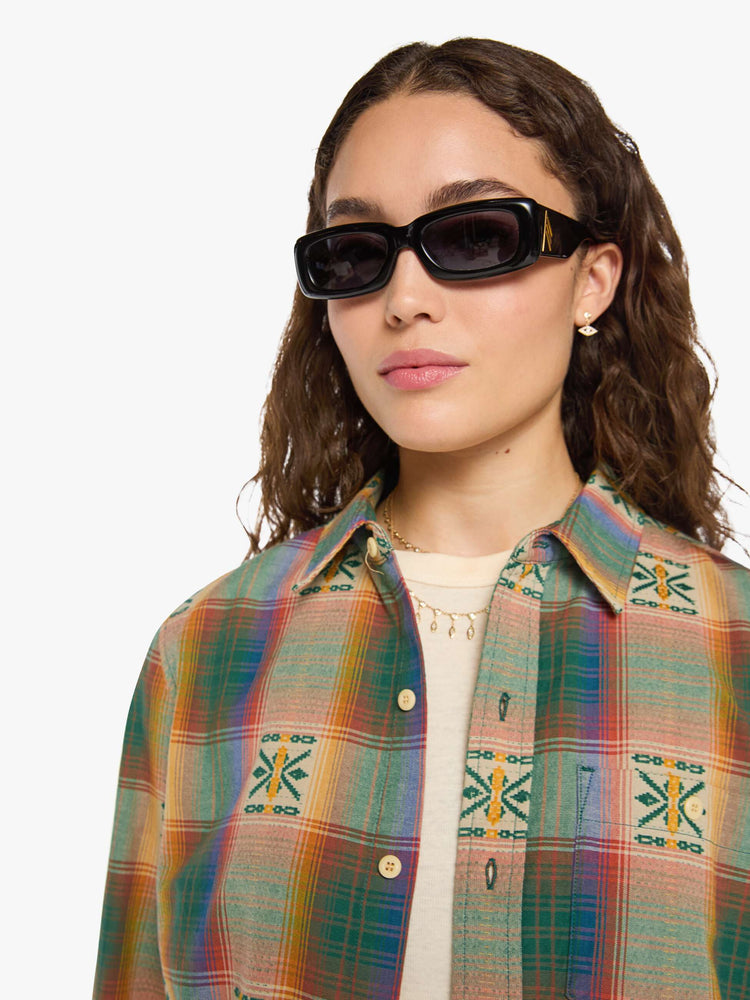 Close up view of a woman in  plaid with embroidered details throughout button up.