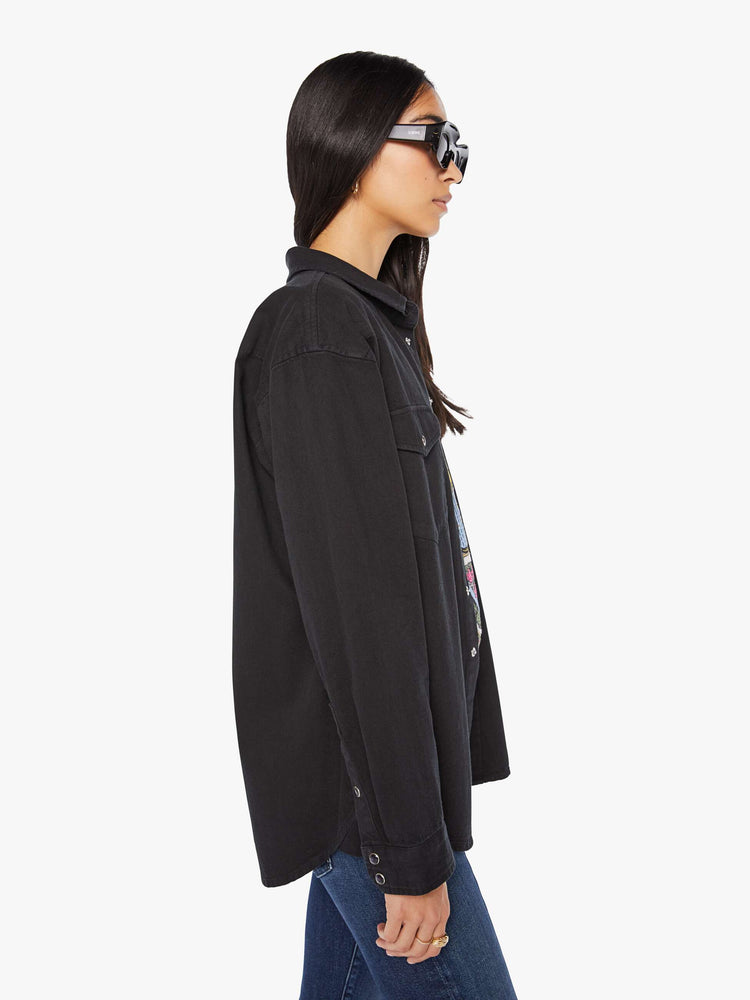 Side view of woman in a black oversized denim button-up with drop shoulders, front patch pockets, a Western-inspired yoke and a curved hem.