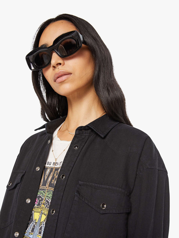 Close up view of woman in a black oversized denim button-up with drop shoulders, front patch pockets, a Western-inspired yoke and a curved hem.