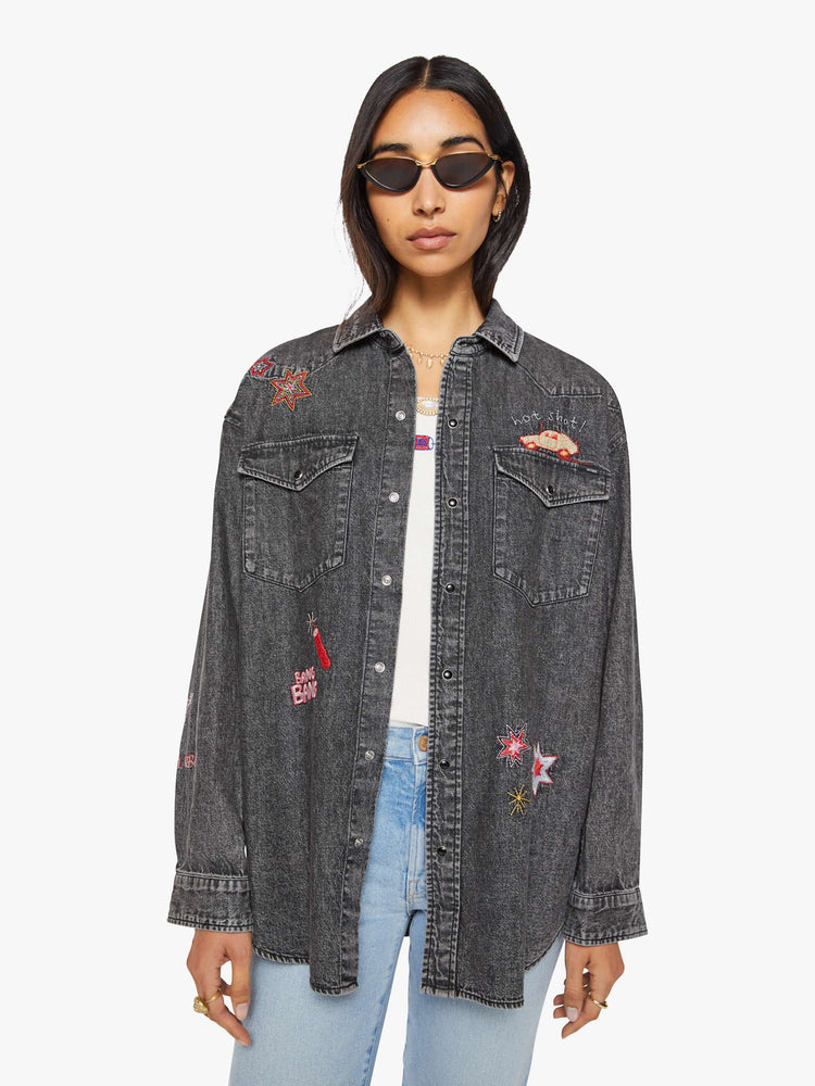 Front view of a woman in a faded dark grey with embroidered graphics throughout  oversized denim button-up with drop shoulders, front patch pockets, a Western-inspired yoke and a curved hem. 