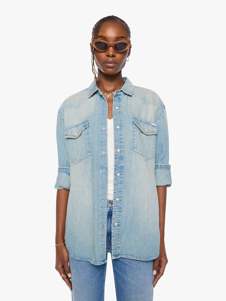 Front view of a woman in a light blue  oversized denim button-up with drop shoulders, front patch pockets, a Western-inspired yoke and a curved hem. 