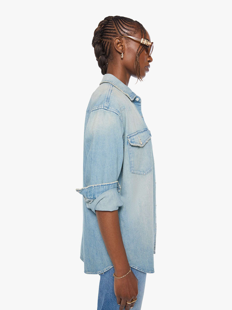 Side view of a woman in a light blue  oversized denim button-up with drop shoulders, front patch pockets, a Western-inspired yoke and a curved hem. 
