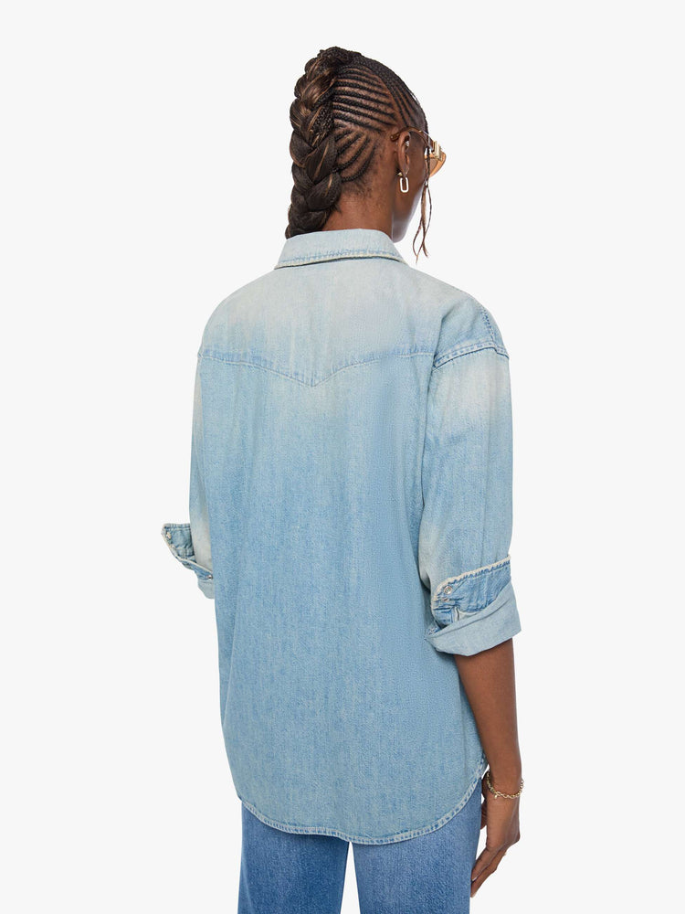 Back view of a woman in a light blue  oversized denim button-up with drop shoulders, front patch pockets, a Western-inspired yoke and a curved hem. 