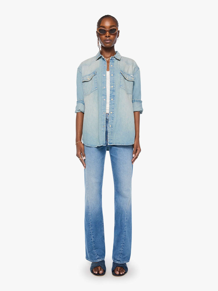 Full body view of a woman in a light blue  oversized denim button-up with drop shoulders, front patch pockets, a Western-inspired yoke and a curved hem. 