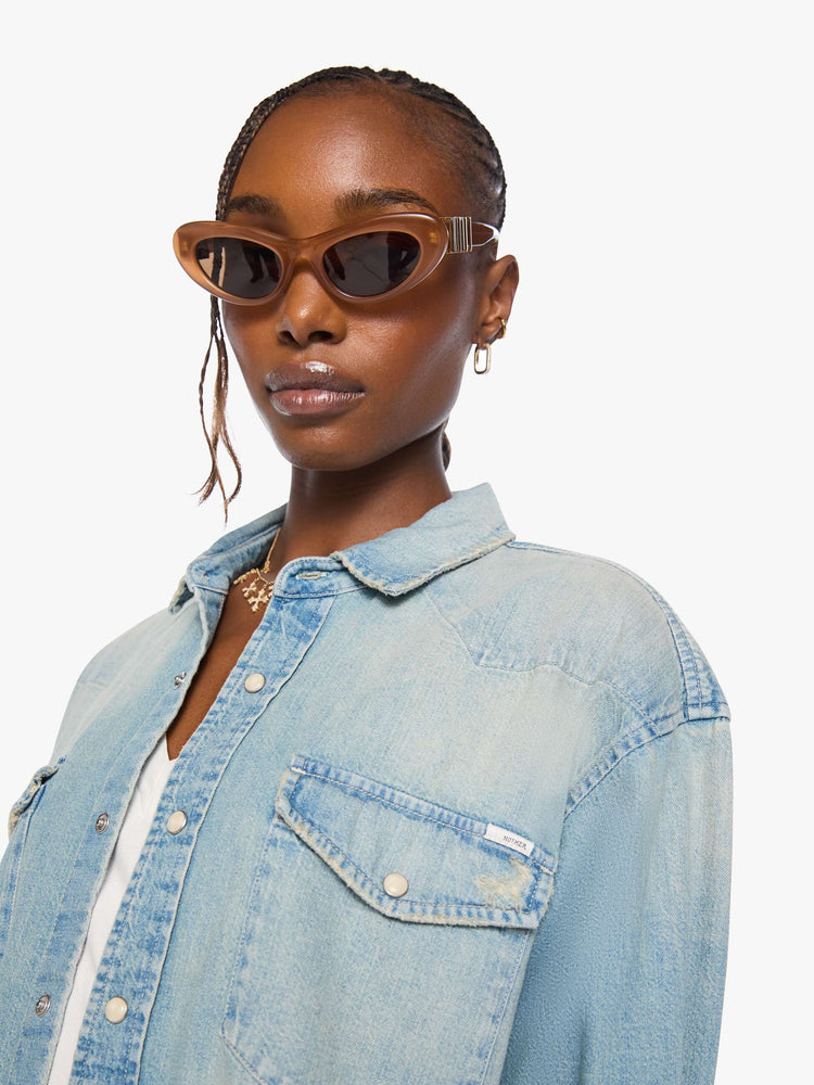Close up view of a woman in a light blue  oversized denim button-up with drop shoulders, front patch pockets, a Western-inspired yoke and a curved hem. 