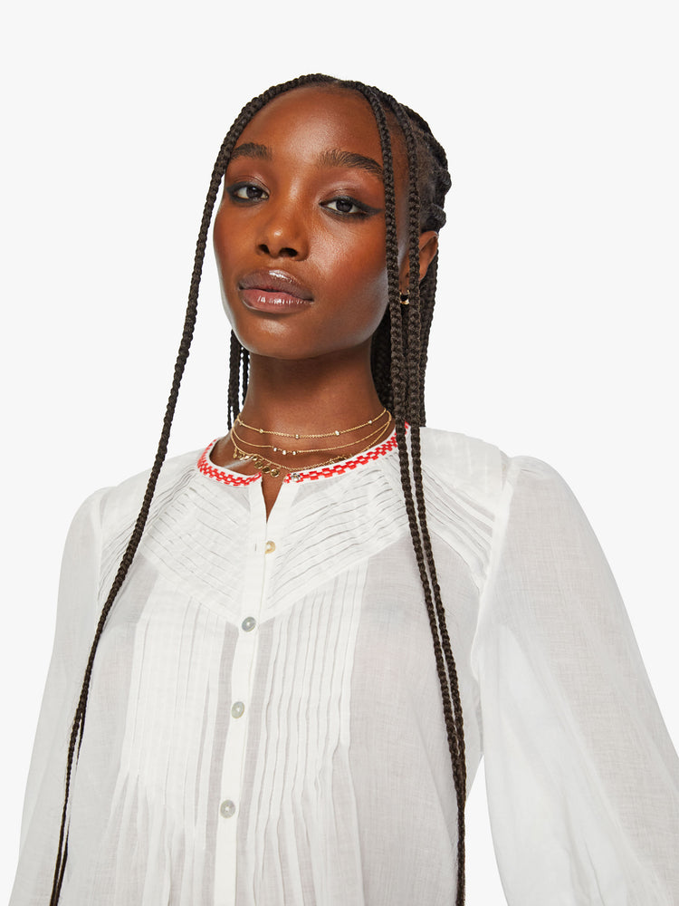 Close up view of a woman white blouse blouse with a crewneck, 3/4-length balloon sleeves, pleated details, buttons down the front and a slightly shrunken fit in white with red trim around the neck and sleeves.