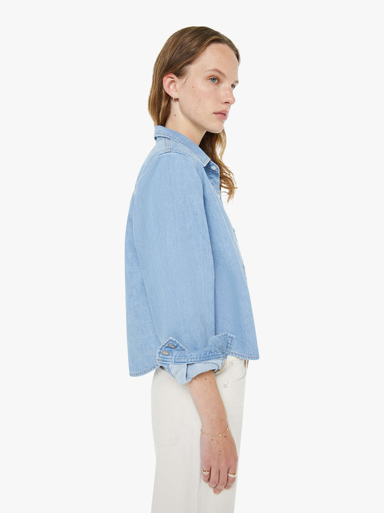 Side view of a woman in a light blue denim classic button-up with a front patch pocket and a cropped fit.