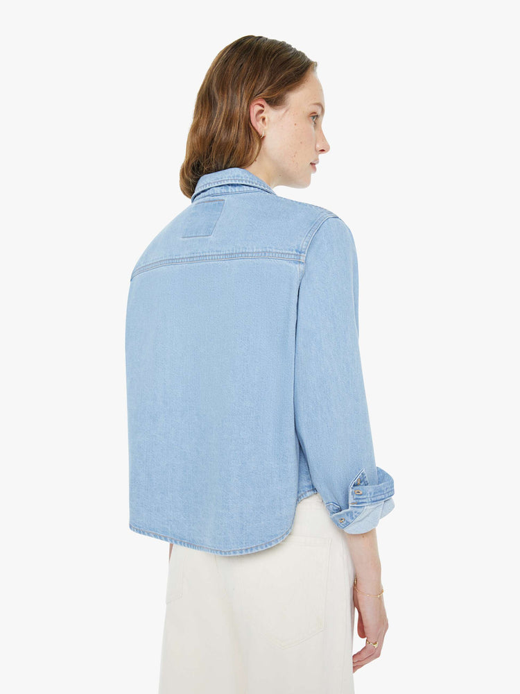 Back view of a woman in a light blue denim classic button-up with a front patch pocket and a cropped fit.