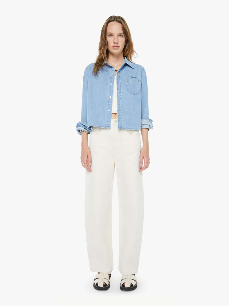 Full body view of a woman in a light blue denim classic button-up with a front patch pocket and a cropped fit.