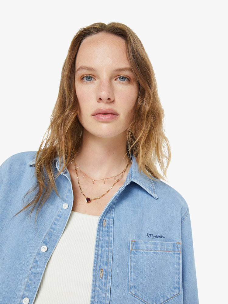 Close up view of a woman in a light blue denim classic button-up with a front patch pocket and a cropped fit.