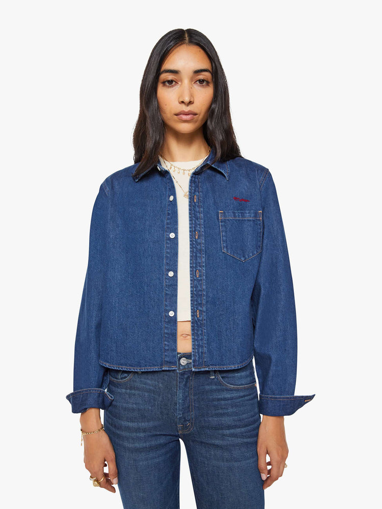 Front view of a woman in a dark blue  cropped button-up shirt with a patch pocket and MOTHER's name embroidered in red on the chest. 