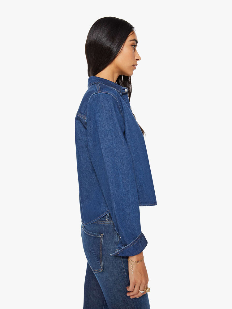 Side view of a woman in a dark blue  cropped button-up shirt with a patch pocket and MOTHER's name embroidered in red on the chest. 