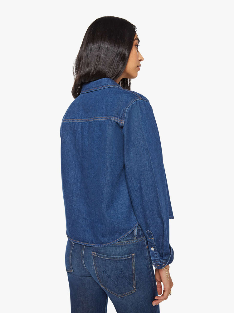 Back view of a woman in a dark blue  cropped button-up shirt with a patch pocket and MOTHER's name embroidered in red on the chest. 