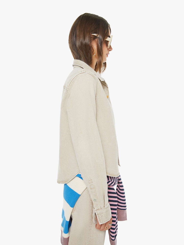 Side view of a woman in faded khaki  button-up denim top with a front patch pocket and a curved, cropped hem.