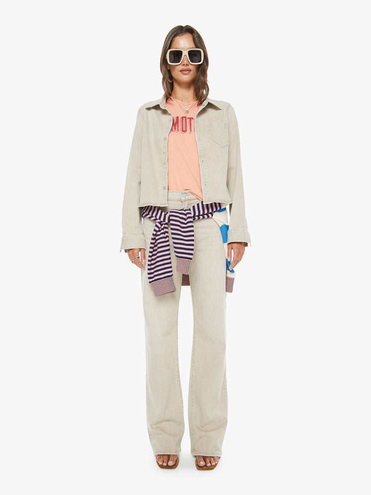 Full body view of a woman in faded khaki  button-up denim top with a front patch pocket and a curved, cropped hem.