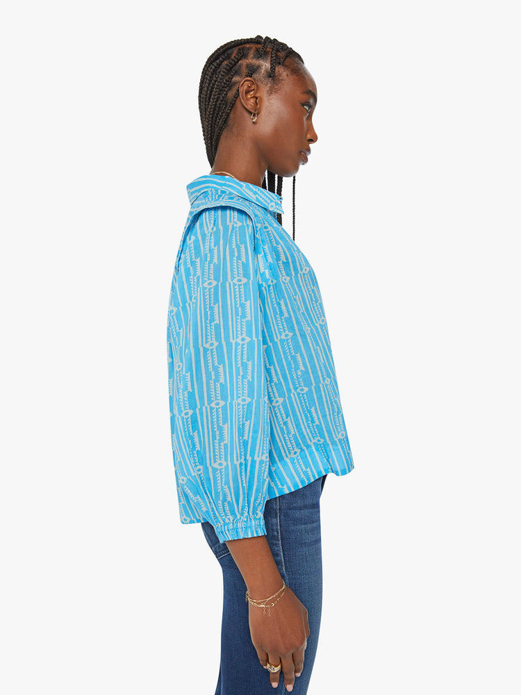 Side view of a woman collared button-up blouse with extra-wide shoulder seams, 3/4-length balloon sleeves and a slightly cropped hem in a light blue with white pattern.