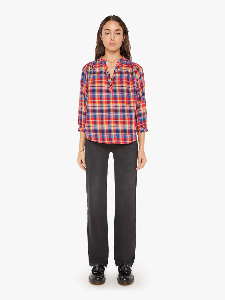 Full body view of a woman hot pink, yellow, and blue plaid lightweight blouse with a buttoned V-neck, 3/4-length balloon sleeves, a curved hem and ruffles throughout for a loose, flowy fit.