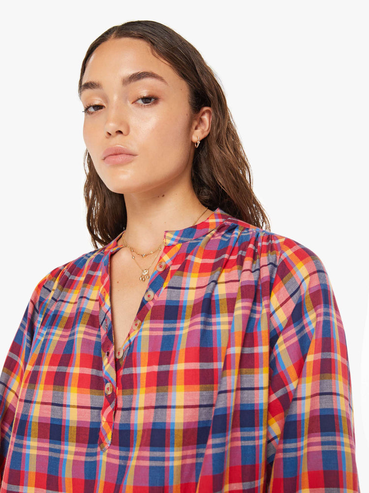 Close up view of a woman hot pink, yellow, and blue plaid lightweight blouse with a buttoned V-neck, 3/4-length balloon sleeves, a curved hem and ruffles throughout for a loose, flowy fit.