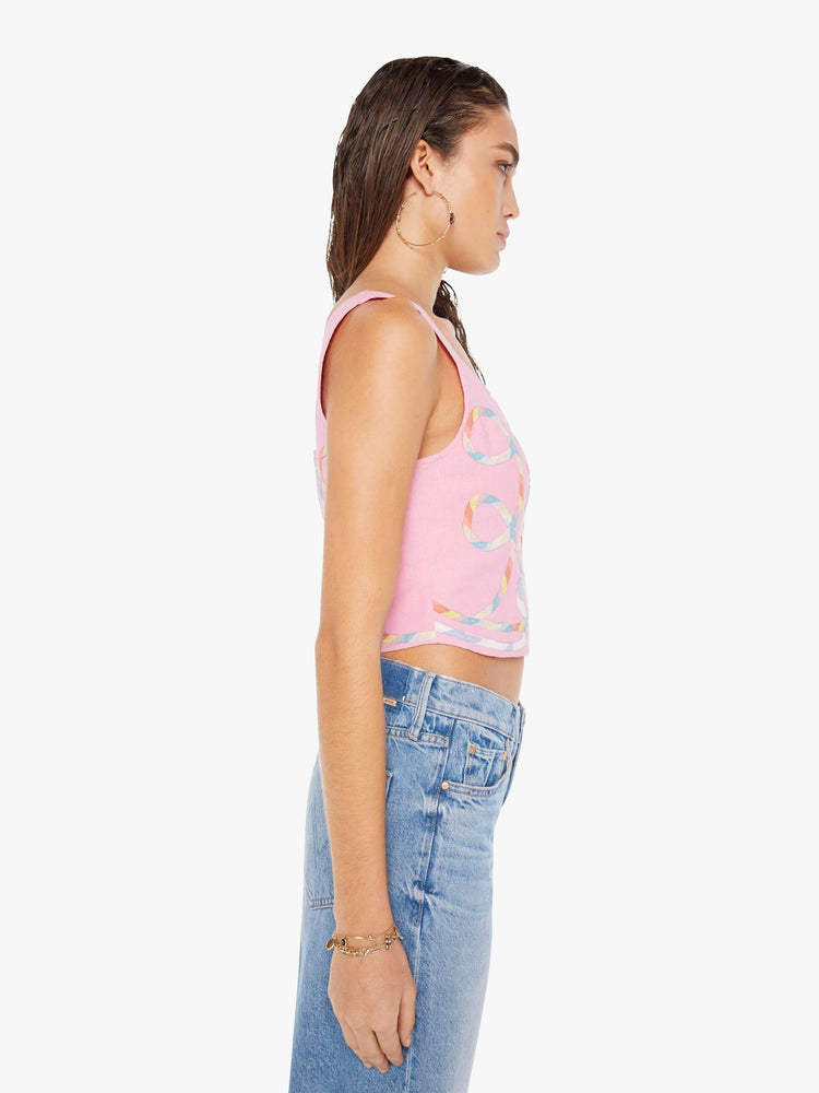 Side view of a woman wearing a pink bustier top featuring multi color ribbon embroidered throughout, paired with a light blue wash denim short.