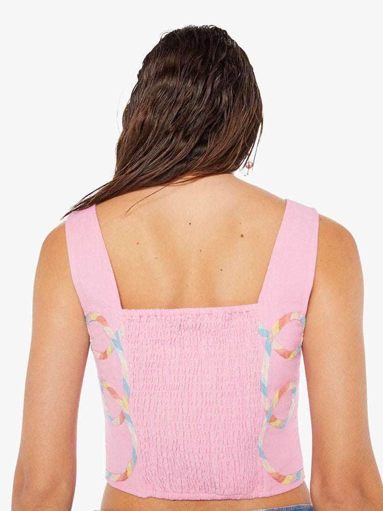 Back close up view of a woman wearing a pink bustier top featuring multi color ribbon embroidered throughout and a rouched elastic back, paired with a light blue wash denim short.