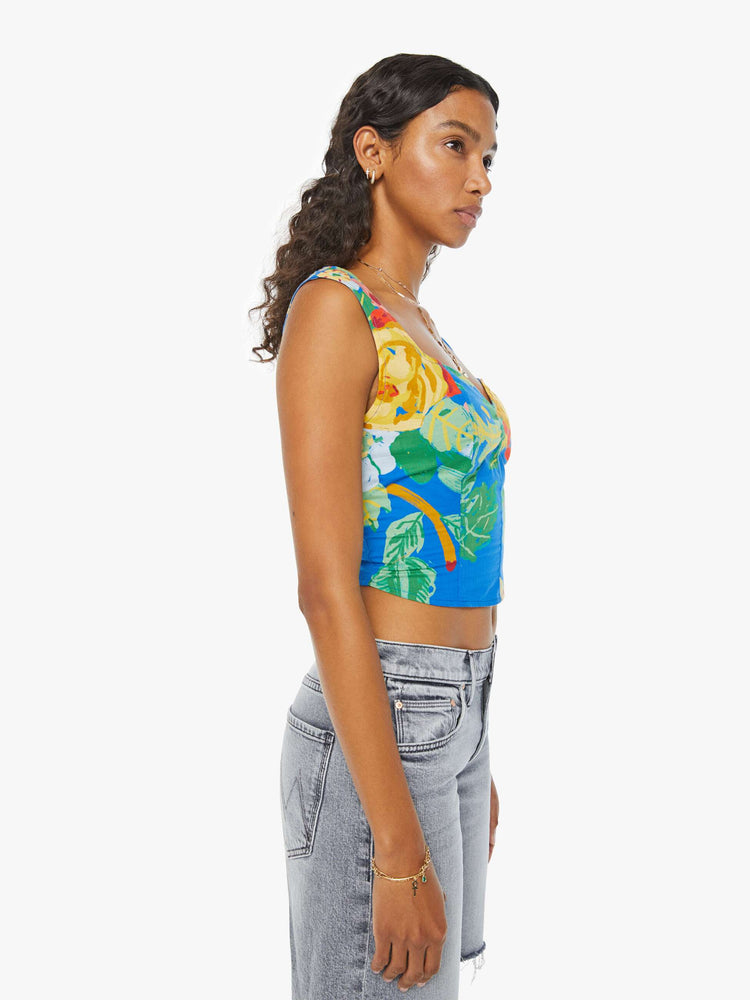 Side view of a woman in a blue sleeveless corset with an oversized tropical floral print, a sweetheart neckline, seamed details, a smocked, elastic back panel and a cropped, narrow fit.  Paired with Grey Shorts.