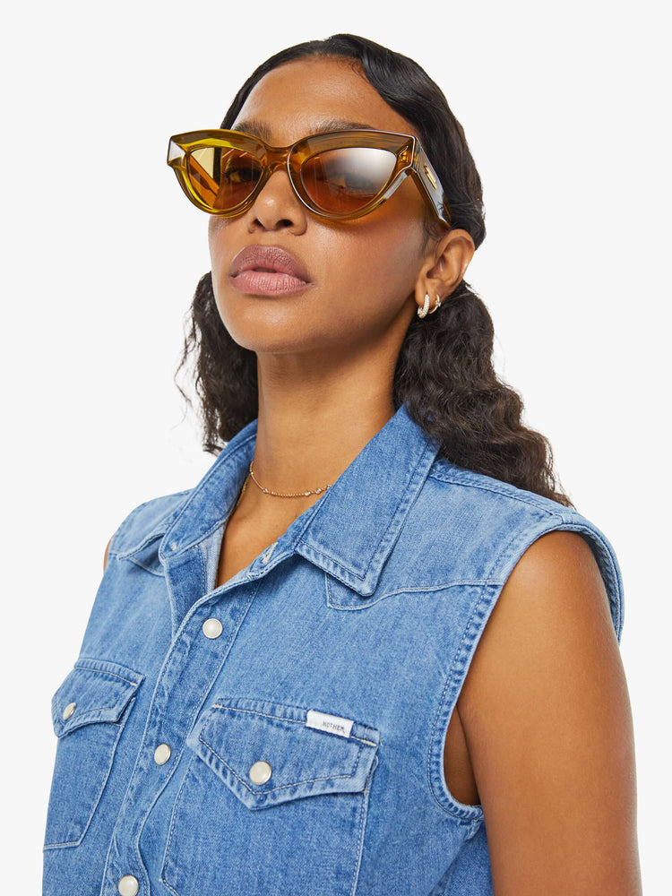 Close up view of a woman medium blue sleeveless button-up with front patch pockets and a cropped hem that ties.